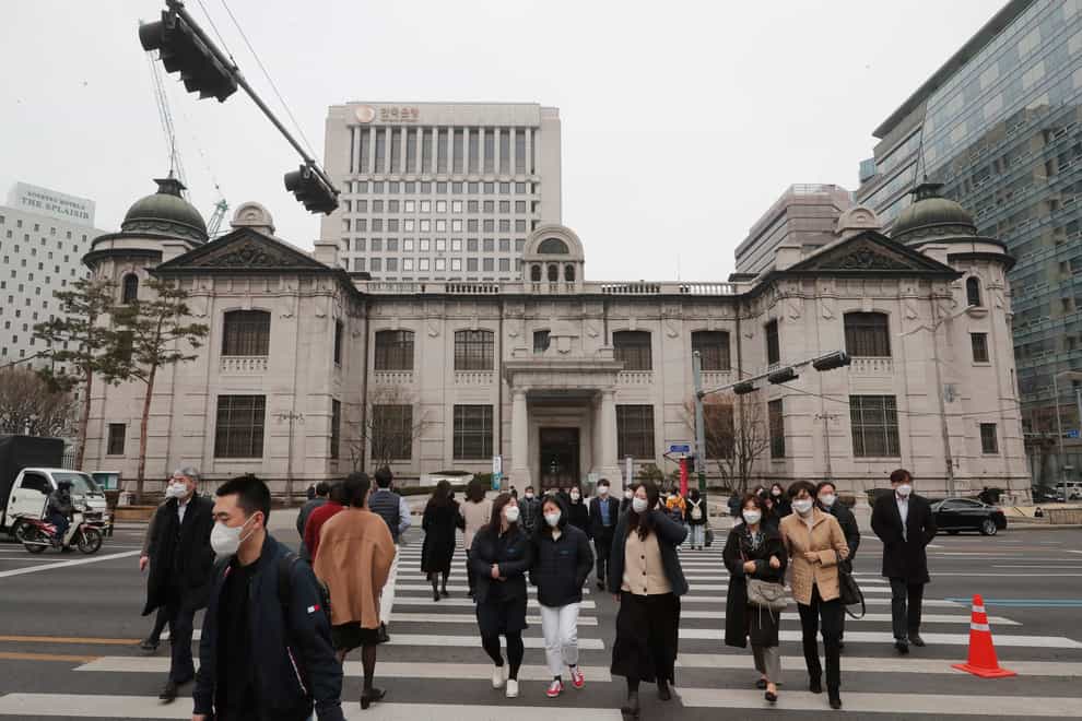 People wearing face masks walk by the headquarters of the Bank of Korea in Seoul, South Korea (Ahn Young-joon/AP)