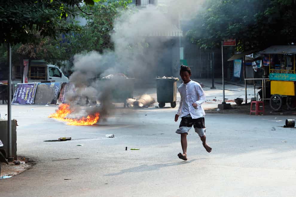 A man crosses the street while fire is seen in front of a road barricade that prevents security forces from advancing in Mandalay, Myanmar (AP)