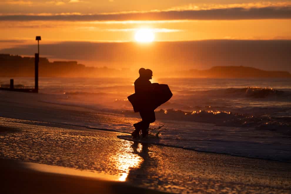 Bodyboarders make their way into the sea as the sun rises over Boscombe beach in Dorset