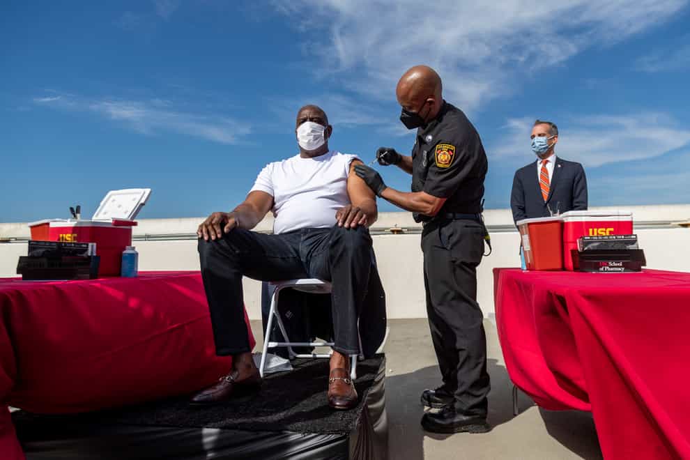 A Los Angeles Fire Department official gives a vaccine shot to former Los Angeles Lakers basketball star Magic Johnson on parking station rooftop clinic at the University of Southern California on Wednesday