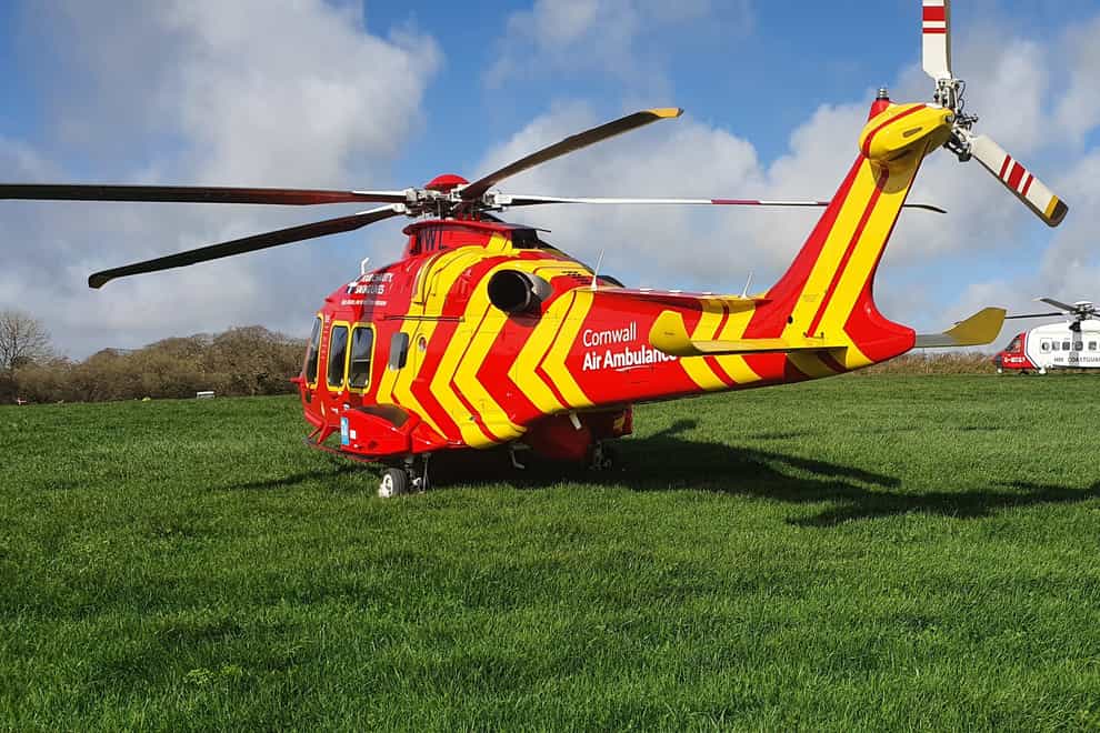 A Cornwall Air Ambulance helicopter alongside a Coastguard SAR helicopter in a field adjacent to where a Royal Navy Hawk jet crashed in woodland in Cornwall
