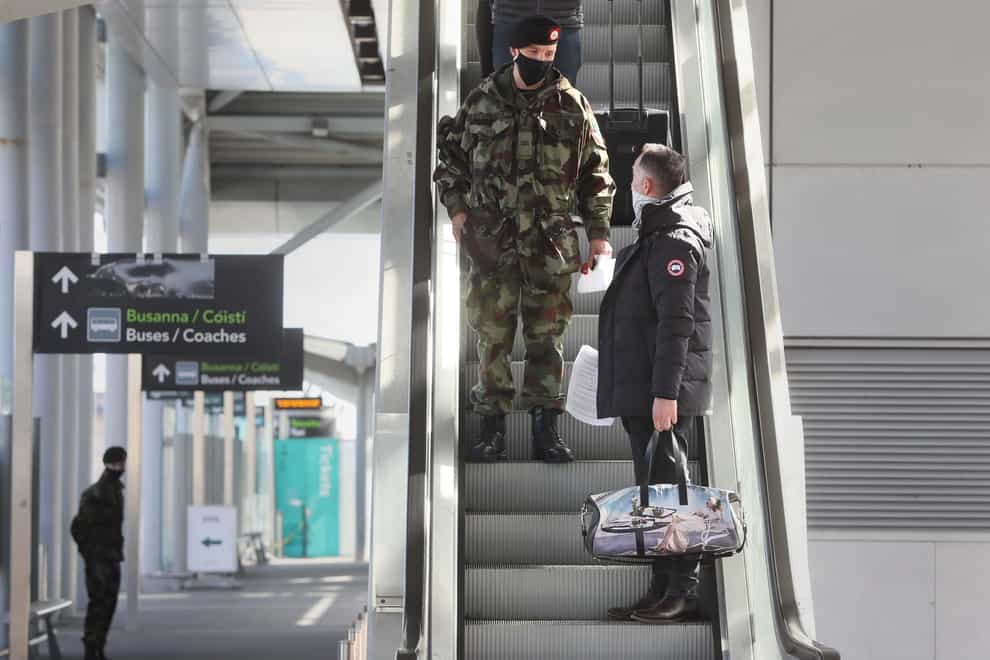 A passenger is escorted to a coach by a member of the defence forces after arriving at Dublin Airport