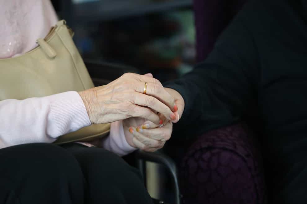 A care home resident holds hand with a family member (Aaron Chown/PA)