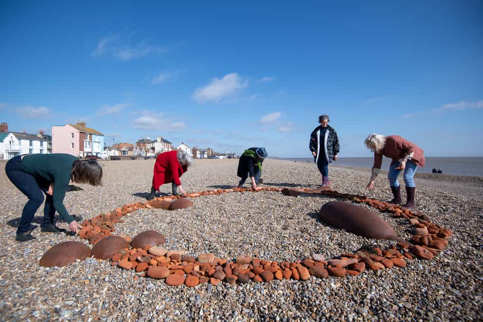 Members of Arts Club Aldeburgh Beach use red sea bricks to incorporate four of sculptor Sir Antony Gormley’s works into a new artwork