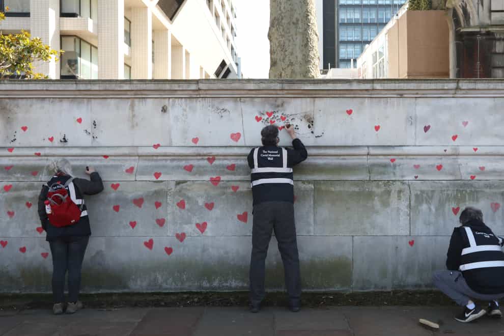 Members of bereaved families paint red hearts on the Covid-19 Memorial Wall