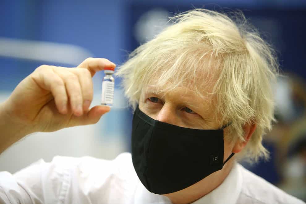 Boris Johnson holds a vial aloft as he wears a face covering