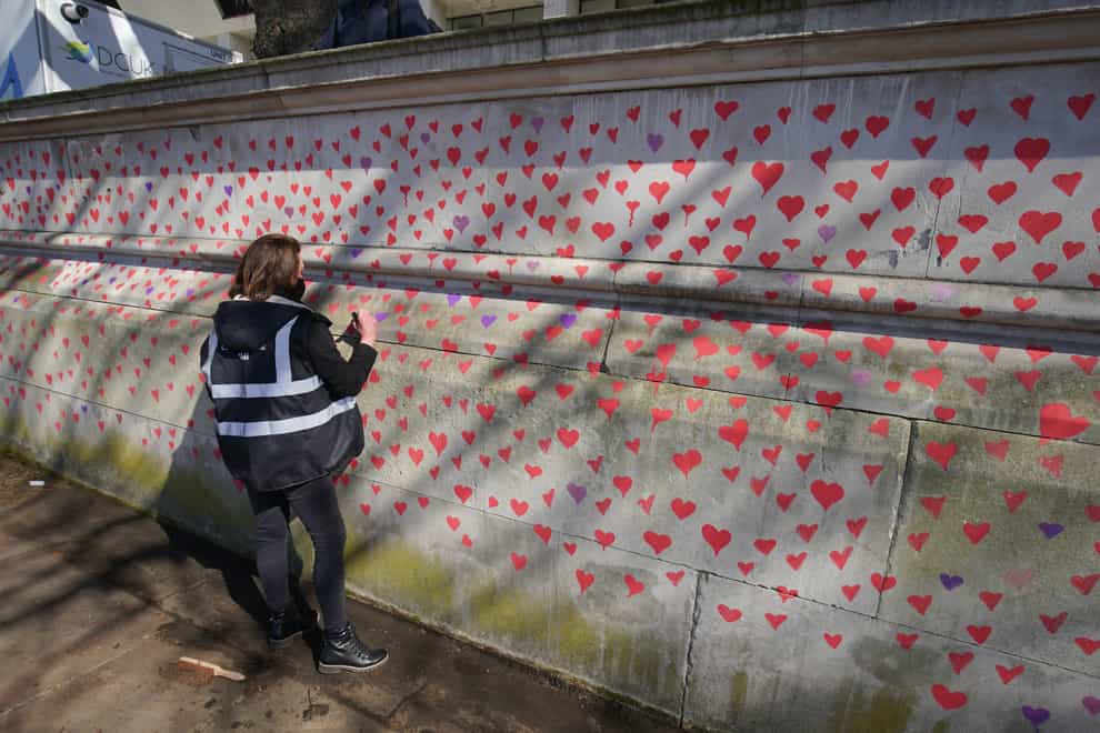 A woman paints red hearts on the Covid-19 memorial wall opposite the Houses of Parliament in central London (Aaron Chown/PA)