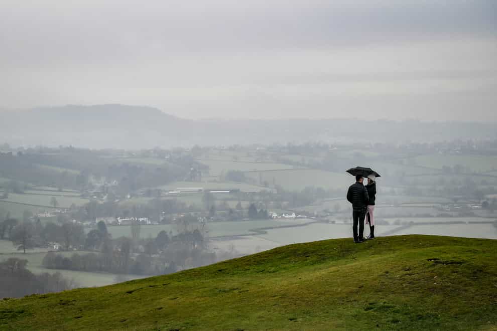 A couple look out on to the misty Cotswold landscape at the top of Frocester Hill, Gloucestershire