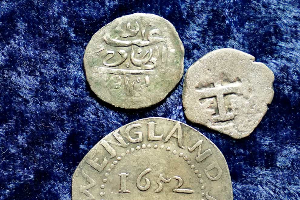 A 17th-century Arabian silver coin, top, that research shows was struck in 1693 in Yemen, rests near an Oak Tree Shilling minted in 1652 by the Massachusetts Bay Colony, below, and a Spanish half real coin from 1727, right, on a table, in Warwick, Rhode Island