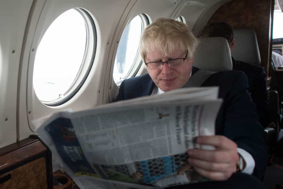 Boris Johnson reads a newspaper while sitting by a window on a plane