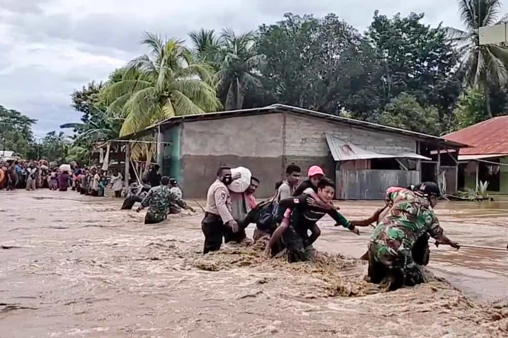 Soldiers and police officers assist residents to cross a flooded road in Indonesia