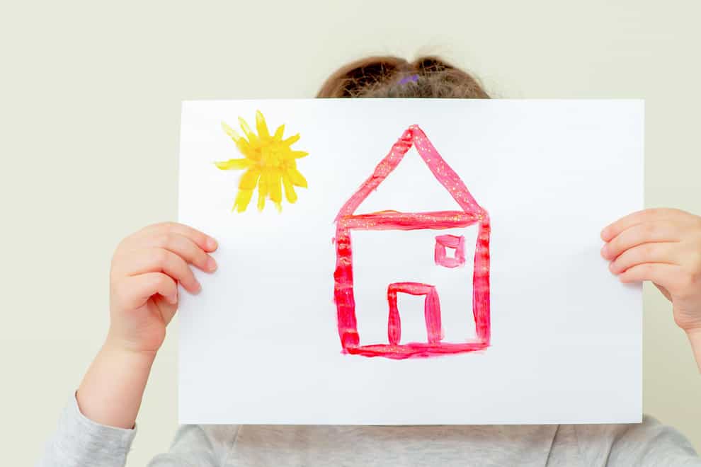 Hands of child holding picture of house covering her face on light background.