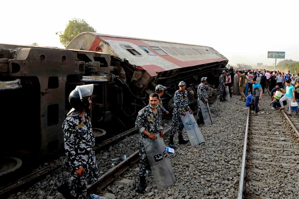 Security forces stand guard as people gather at the site where a passenger train derailed near Banha, Qalyubia province, Egypt (Tarek Wagih/AP)
