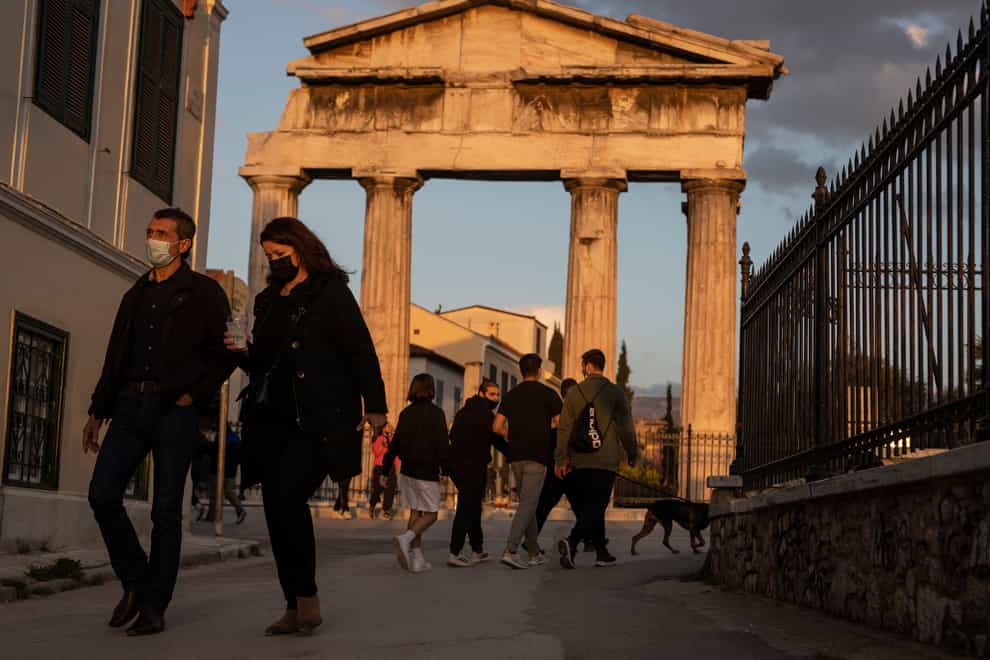 People wearing face masks walk in front of the Gate of the Ancient Roman Agora in the Plaka district of Athens