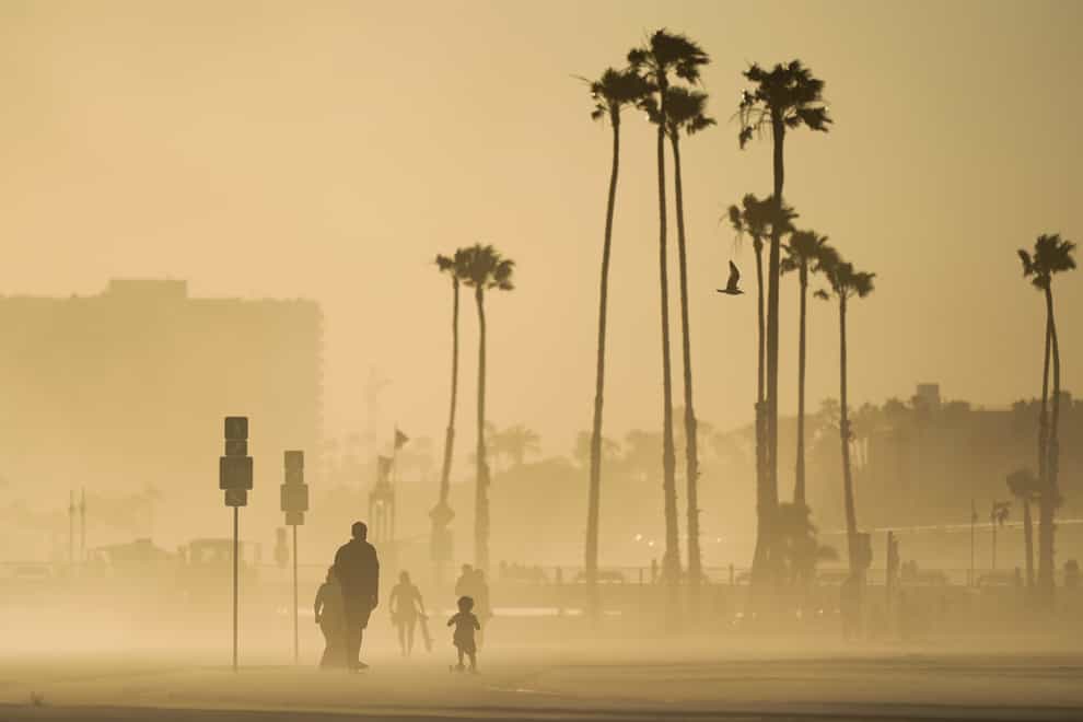 People walk and skateboard on a beach path as evening winds kick up sand in Long Beach, California (Ashley Landis/AP)