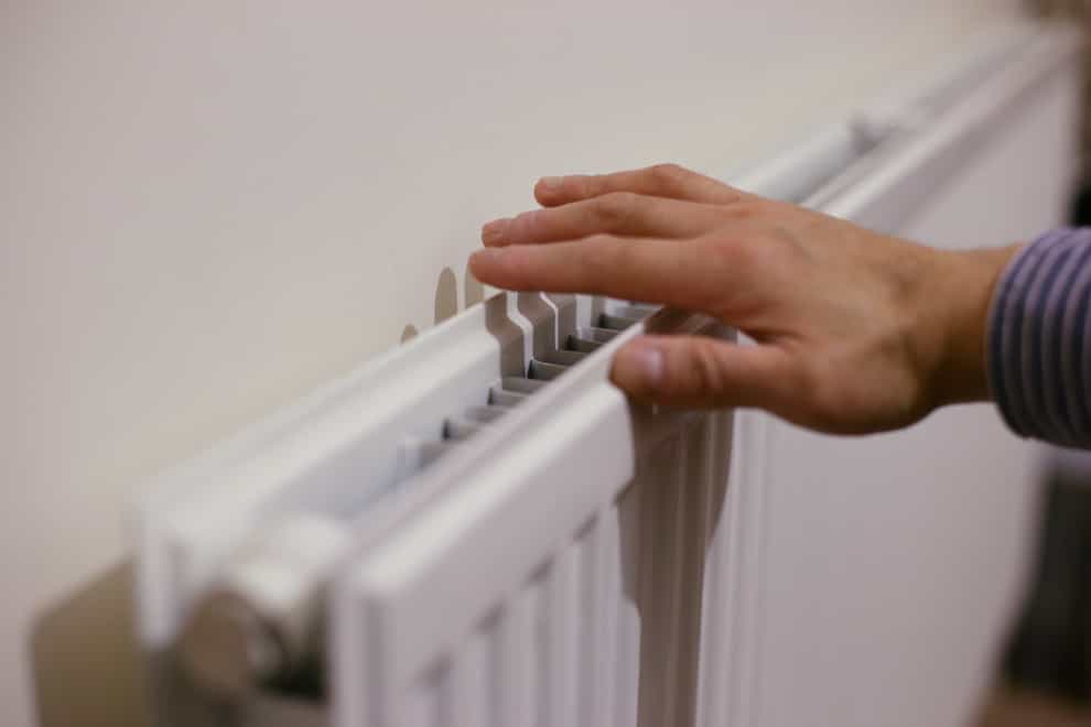 A person feels the warmth from a radiator at a home.