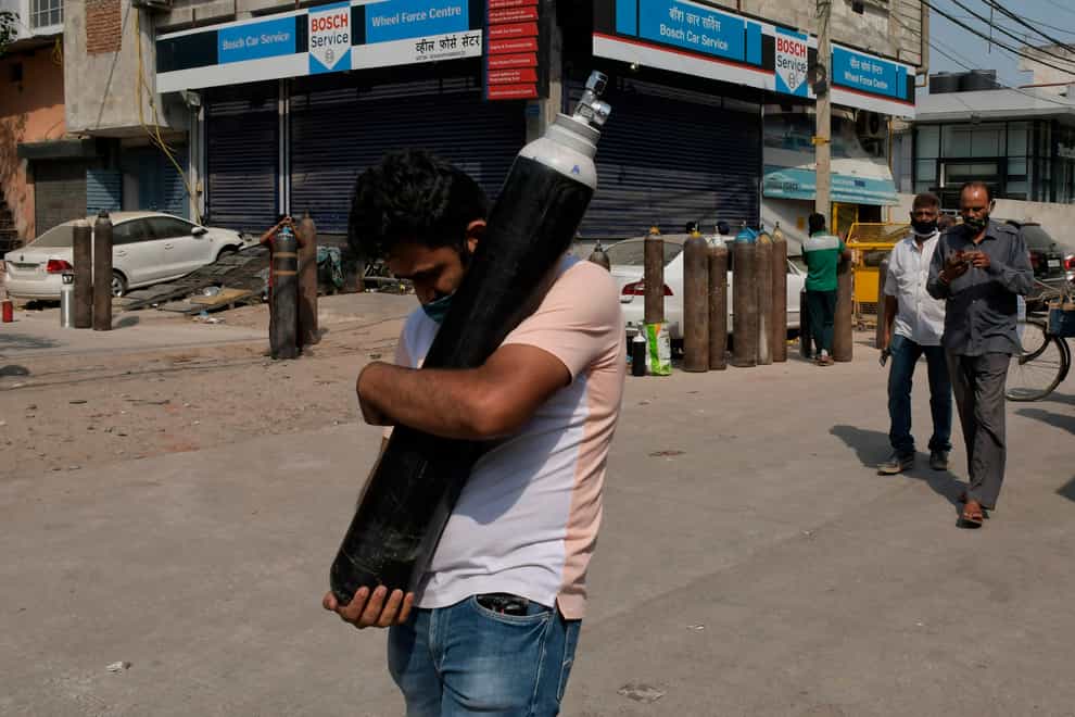 A man walks carrying a refilled cylinder as family members of Covid-19 patients wait in queue to refill their oxygen cylinders at Mayapuri area in New Delhi, India