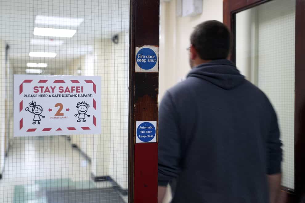 A person walks past a social distancing sign in a corridor at a school