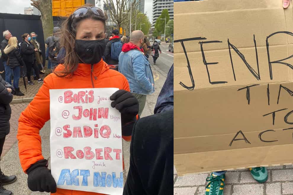 Protesters in Tower Hamlets hold signs. A woman in an orange coat with a black mask and sunglasses on her head holds a sign asking politicians to 'Act Now', while the sign to the right says 'Jenrick Time To Act!'