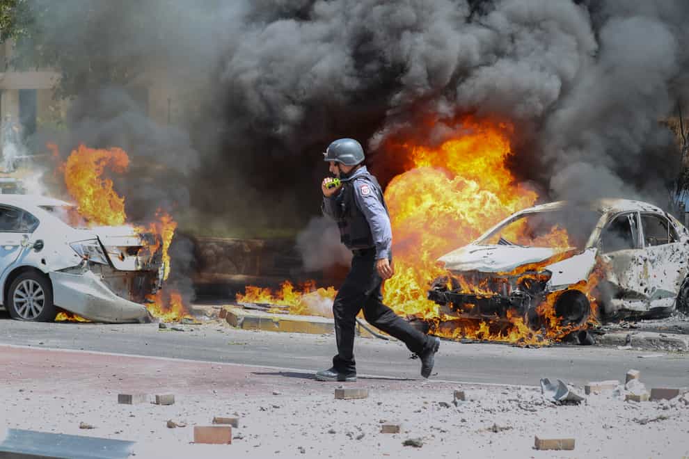 An Israeli firefighter walks next to cars hit by a missile fired from the Gaza Strip in the southern Israeli city of Ashkelon