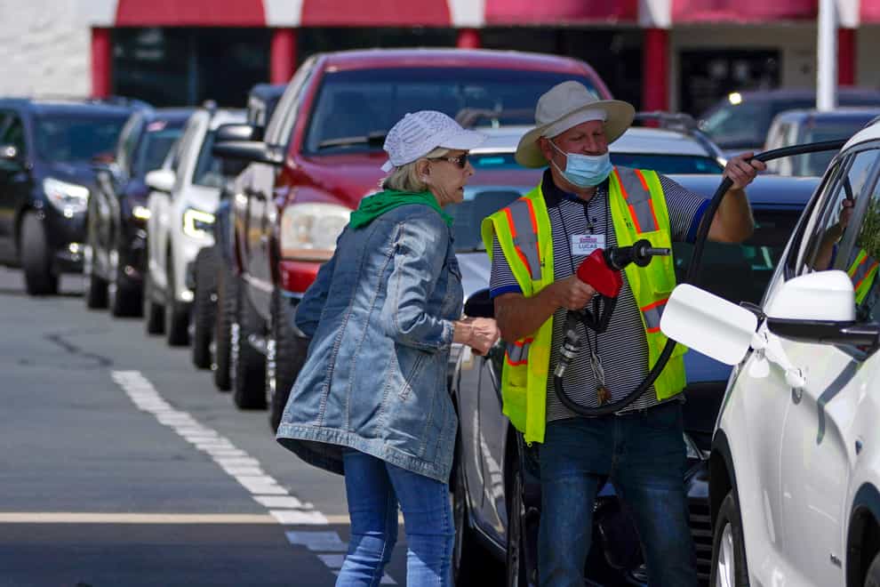 A customer helps pumping gas at Costco, as other wait in line