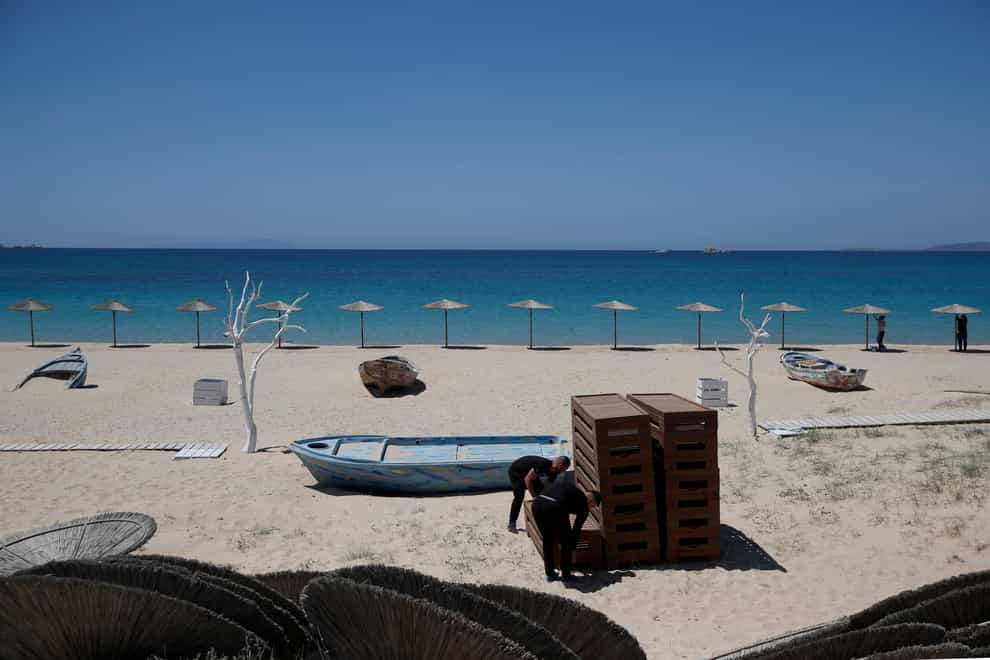 Workers arrange sunbeds as others install umbrellas at Plaka beach on the Aegean island of Naxos, Greece