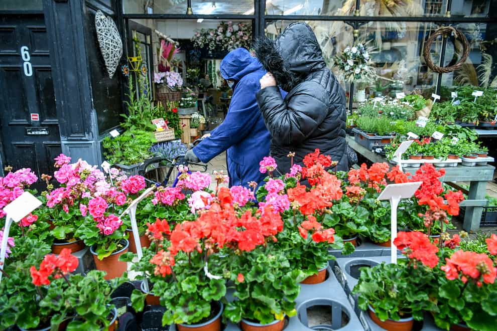 People walk past a florist as they pull their hoods over their heads in Porthcawl, Wales (Ben Birchall/PA)