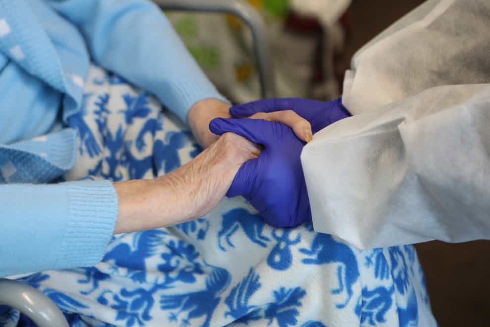 A care home resident and her daughter hold hands during a visit
