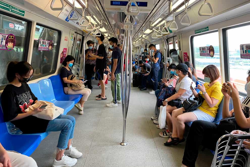 Commuters wear face masks and practise social distancing while onboard an underground train in Singapore (Zen Soo/AP)