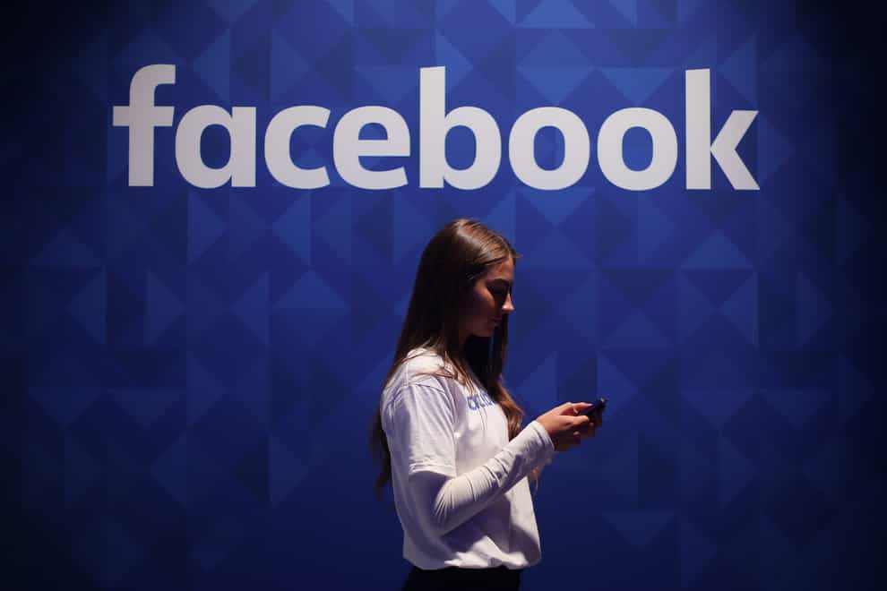A woman using her phone under a logo of Facebook