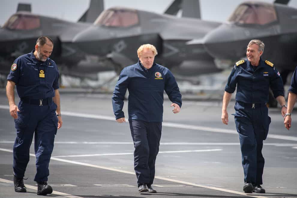 Prime Minister Boris Johnson, along with Commodore Steve Moorhouse and First Sea Lord Admiral Tony Radakin, face strong winds as they walk on the flight deck during a visit aboard HMS Queen Elizabeth in Portsmouth