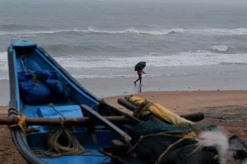 A man walks holding an umbrella on a beach on the Bay of Bengal coast in Odisha, India
