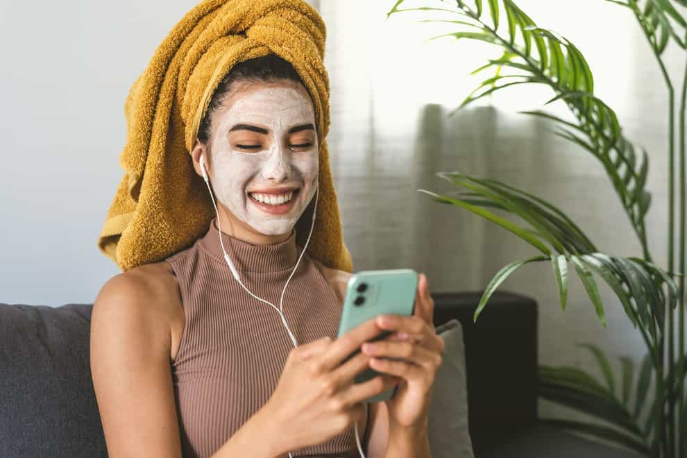 Woman with a skincare face mask on looking at her phone