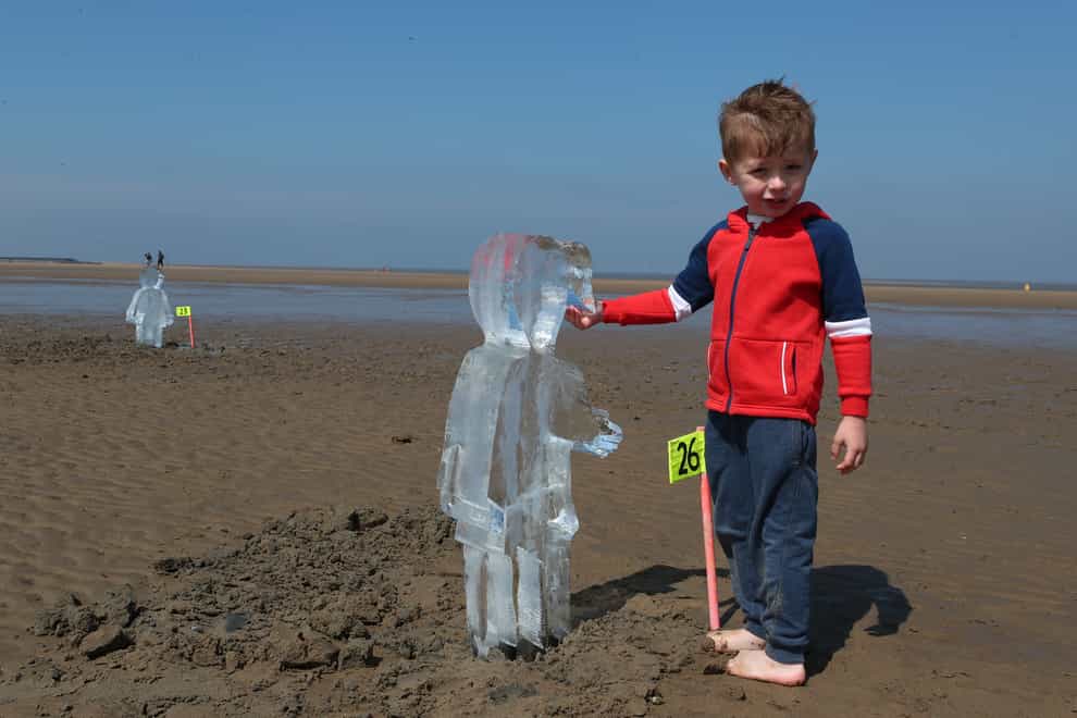 Toby Heptinstall, three, looks at one of 26 ice sculptures of children installed on New Brighton Beach, Wallasey in Merseyside