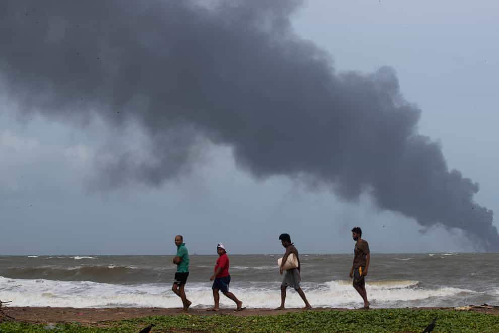 Impoverished Sri Lankans walk along the beach as they try to salvage wreckage washed off to the shore from the burning Singaporean ship MV X-Press Pearl (Eranga Jayawardena/AP)