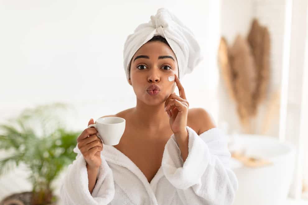 Woman applying face cream and holding a cup of tea