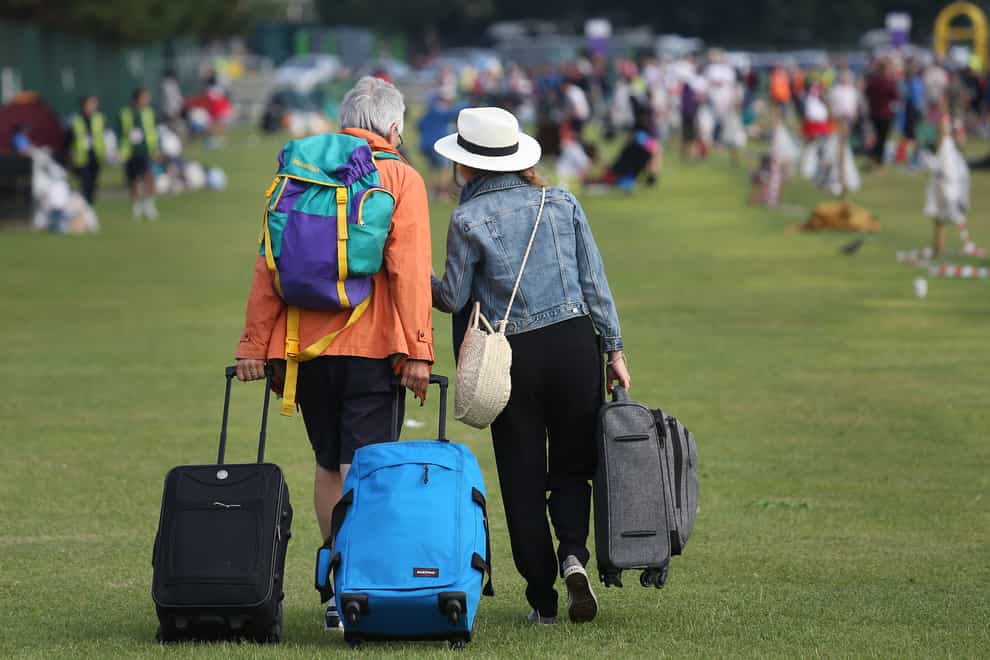 A man and woman pull suitcases across grass