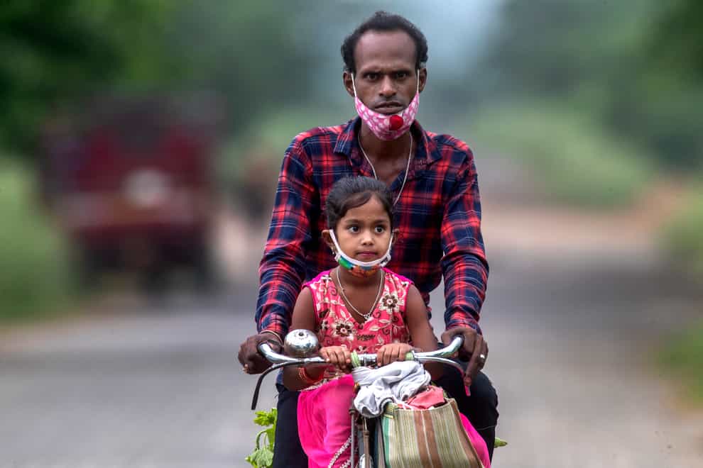 An Indian villager and a child wearing masks ride on a bicycle on the outskirts of Gauhati, India