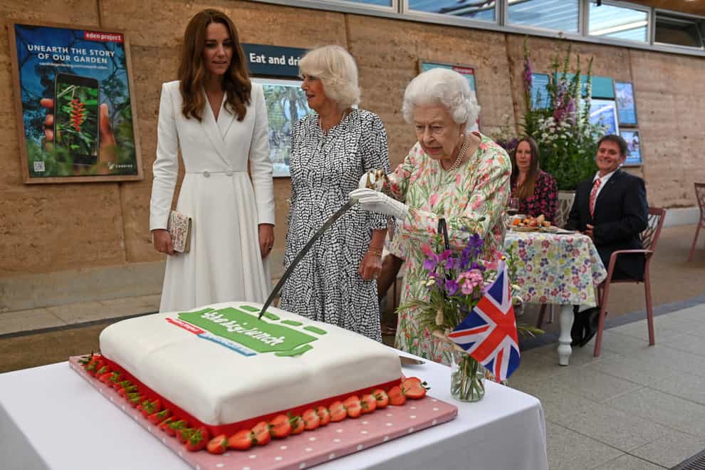 The Duchesses of Cambridge and Cornwall watch as the Queen cuts the cake with a sword