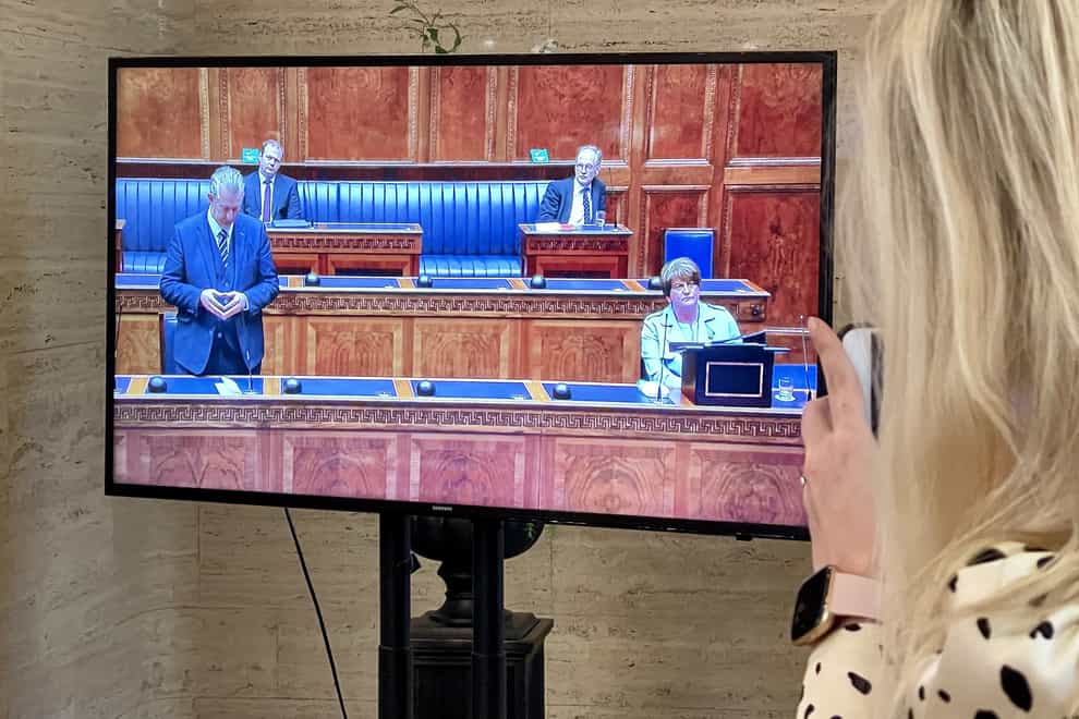 A woman watches a television screen showing DUP leader Edwin Poots (left) in the Stormont Assembly at Parliament Buildings in Belfast pays tribute to Arlene Foster