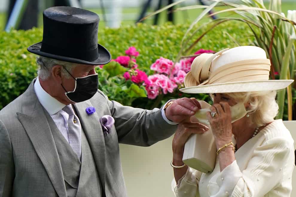 The Prince of Wales helps the Duchess of Cornwall with her mask during day two of Royal Ascot at Ascot Racecourse (Andrew Matthews/PA)