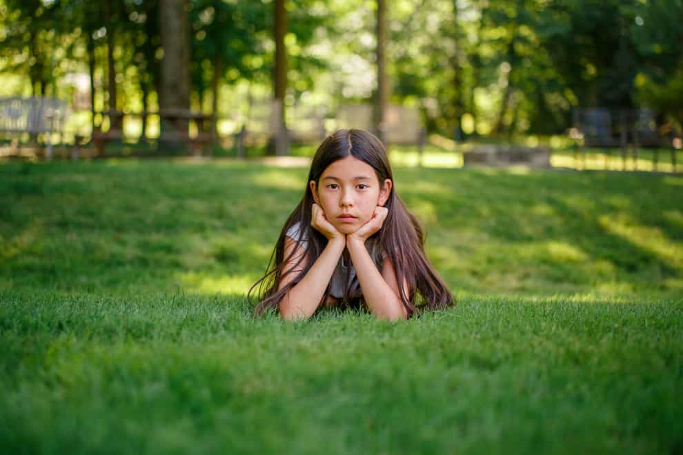 A tween girl lays in the grass with her head propped in her hands