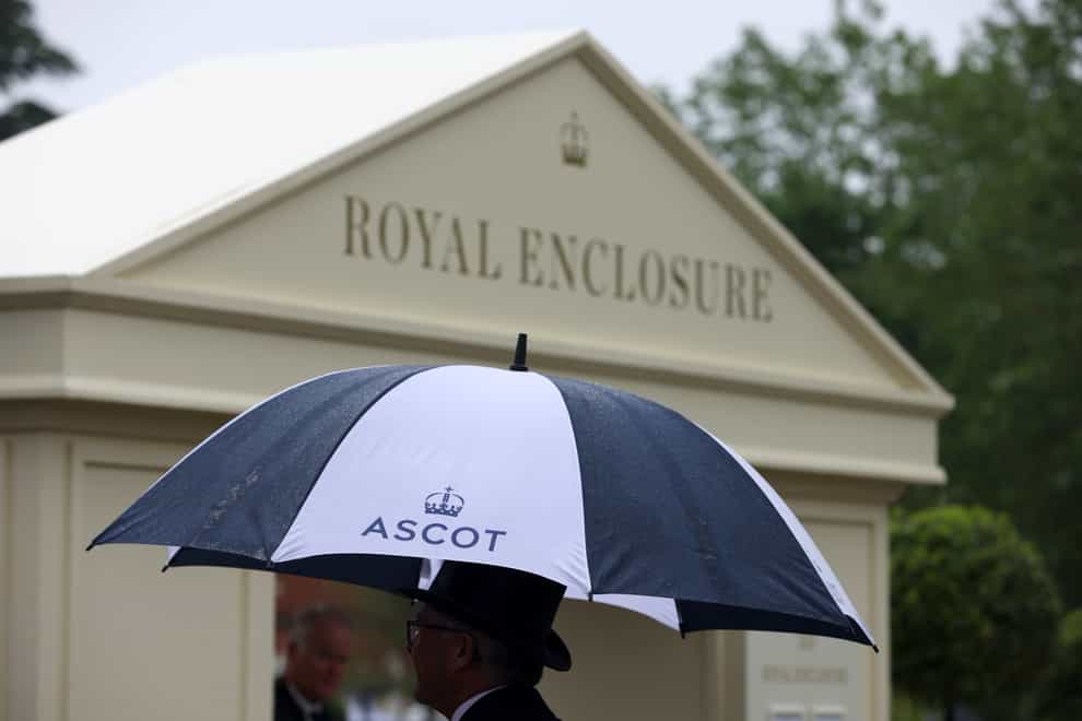 A racegoer takes cover from the heavy rain under an umbrella during day four of Royal Ascot