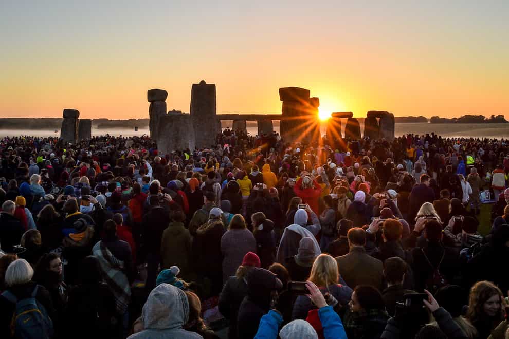 The sun rises between the stones and over crowds at Stonehenge where people gather to celebrate the dawn of the longest day in the UK (Ben Birchall/PA)