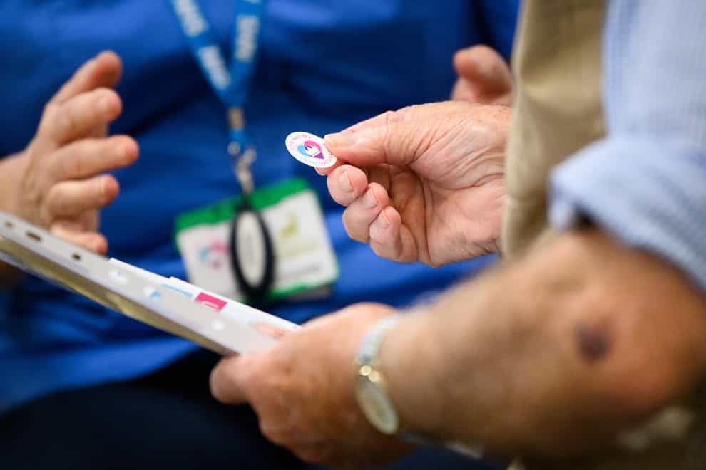 A member of the medical team hands out a sticker reading "I've had my Covid vaccination" at a NHS vaccination centre