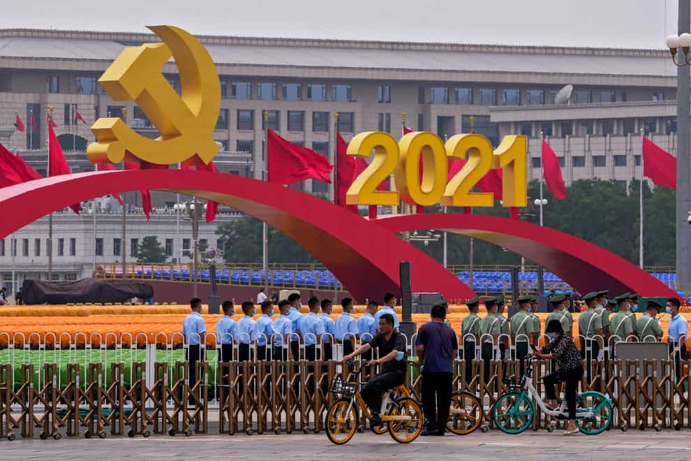 People cycle past Chinese paramilitary police standing in formation near seating and a platform with a Communist Party’s logo setup on Tiananmen Square in Beijing (Andy Wong/PA)