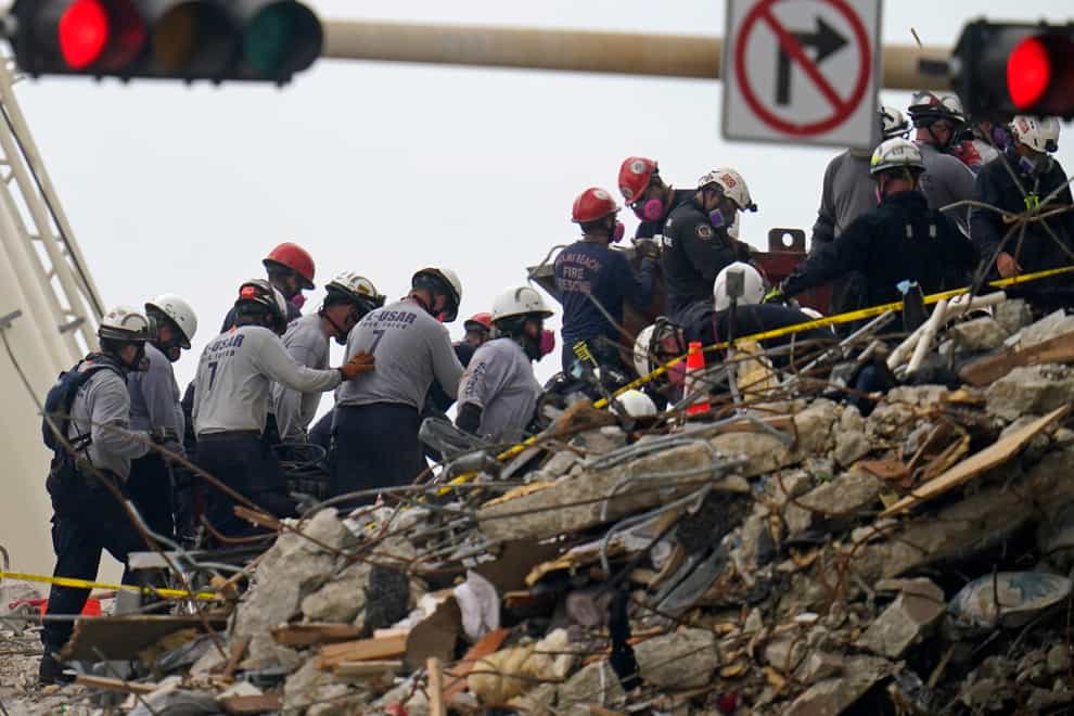 Search and rescue workers carry equipment onto the rubble of an oceanfront condo building that collapsed the week before