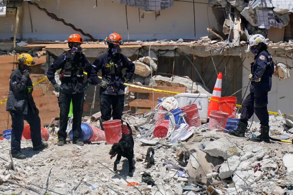 A dog assists search and rescue personnel atop the rubble at the Champlain Towers South condo building