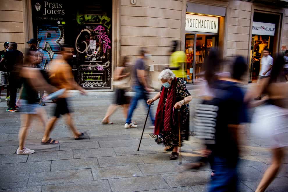 A woman wearing a a face mask to protect against the spread of coronavirus helping himself with a stick to walk walk along a street in Barcelona, Spai (Joan Mateu/AP)