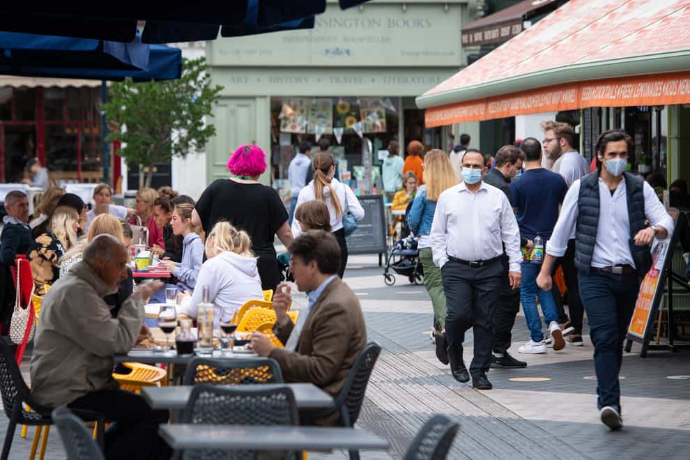 People wearing face coverings pass diners at outside tables in Kensington